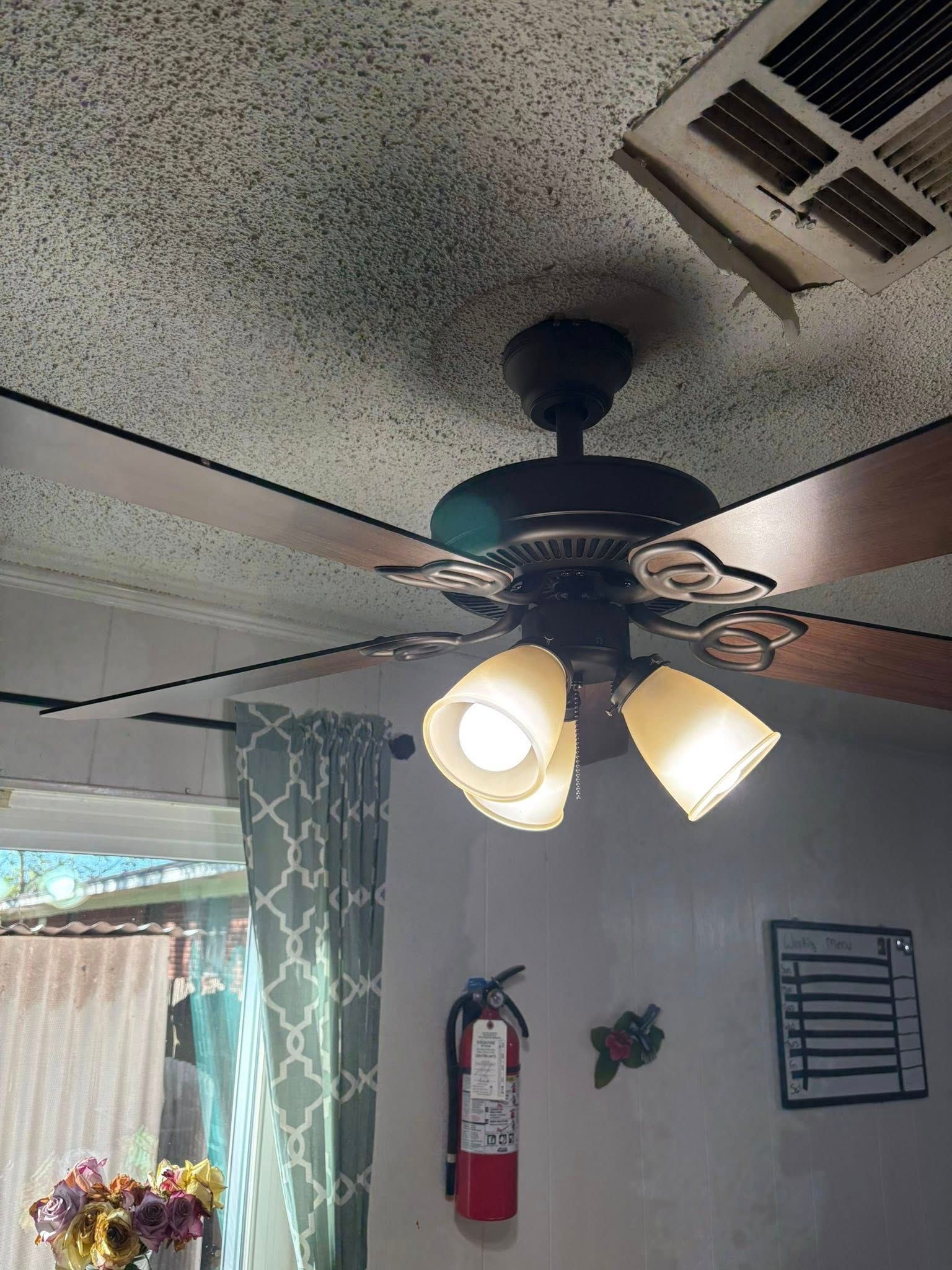 Ceiling fan with lights, textured ceiling, fire extinguisher, window with curtain.
