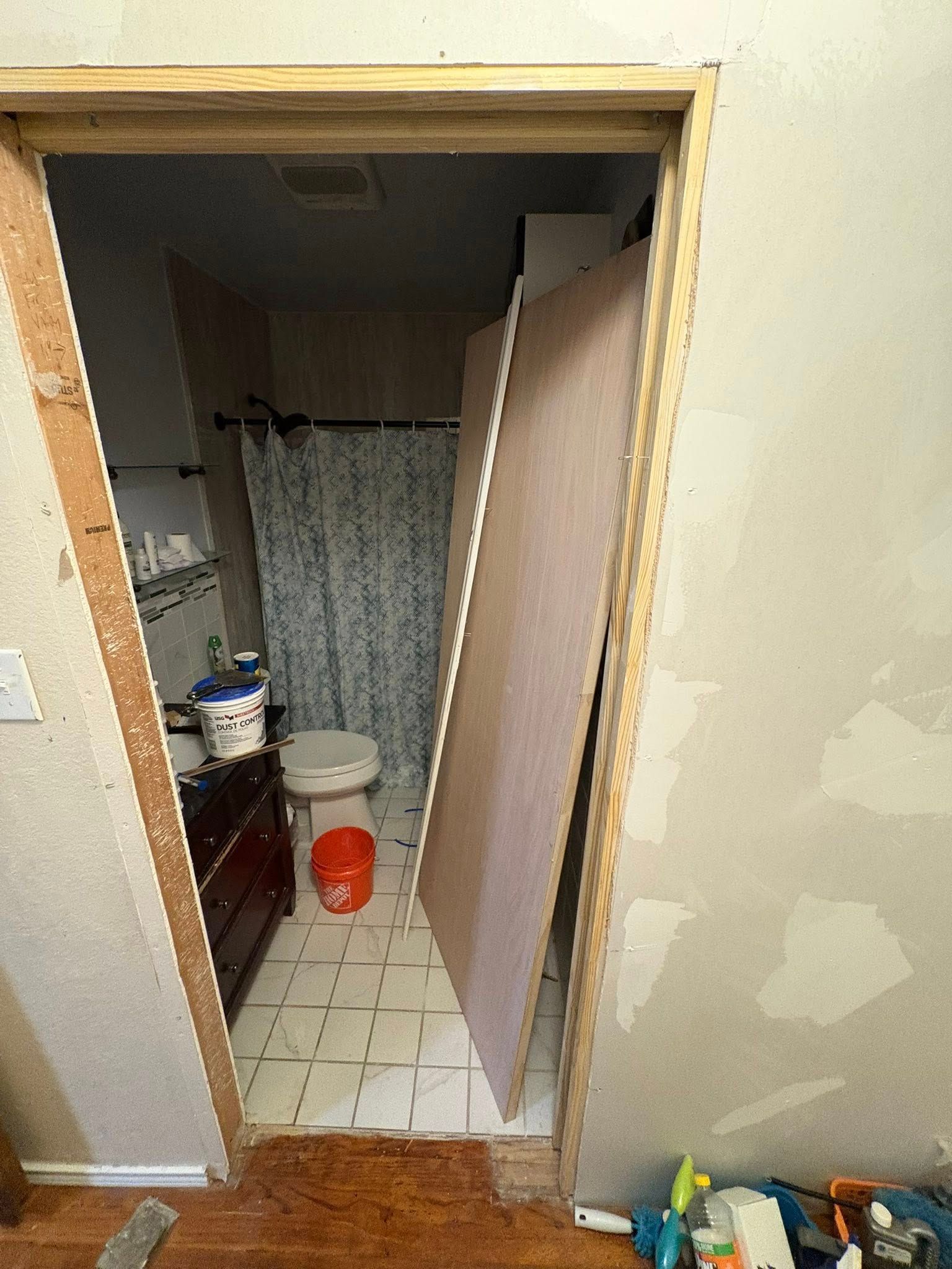 Bathroom doorway undergoing renovation, with a large panel leaning against the opening, interior visible.