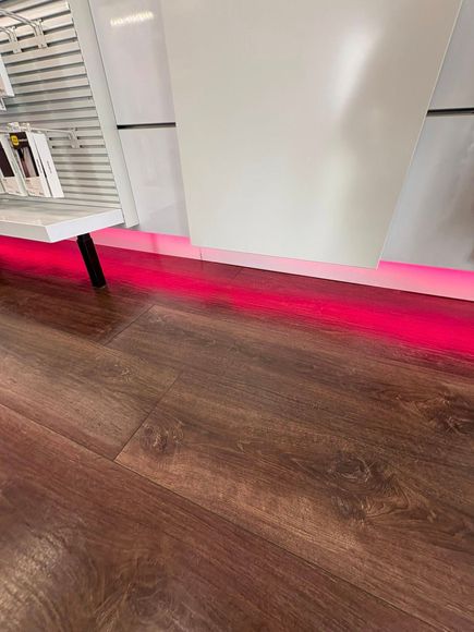 Brown floor with a red light illuminating the base of a display shelf and a white wall.