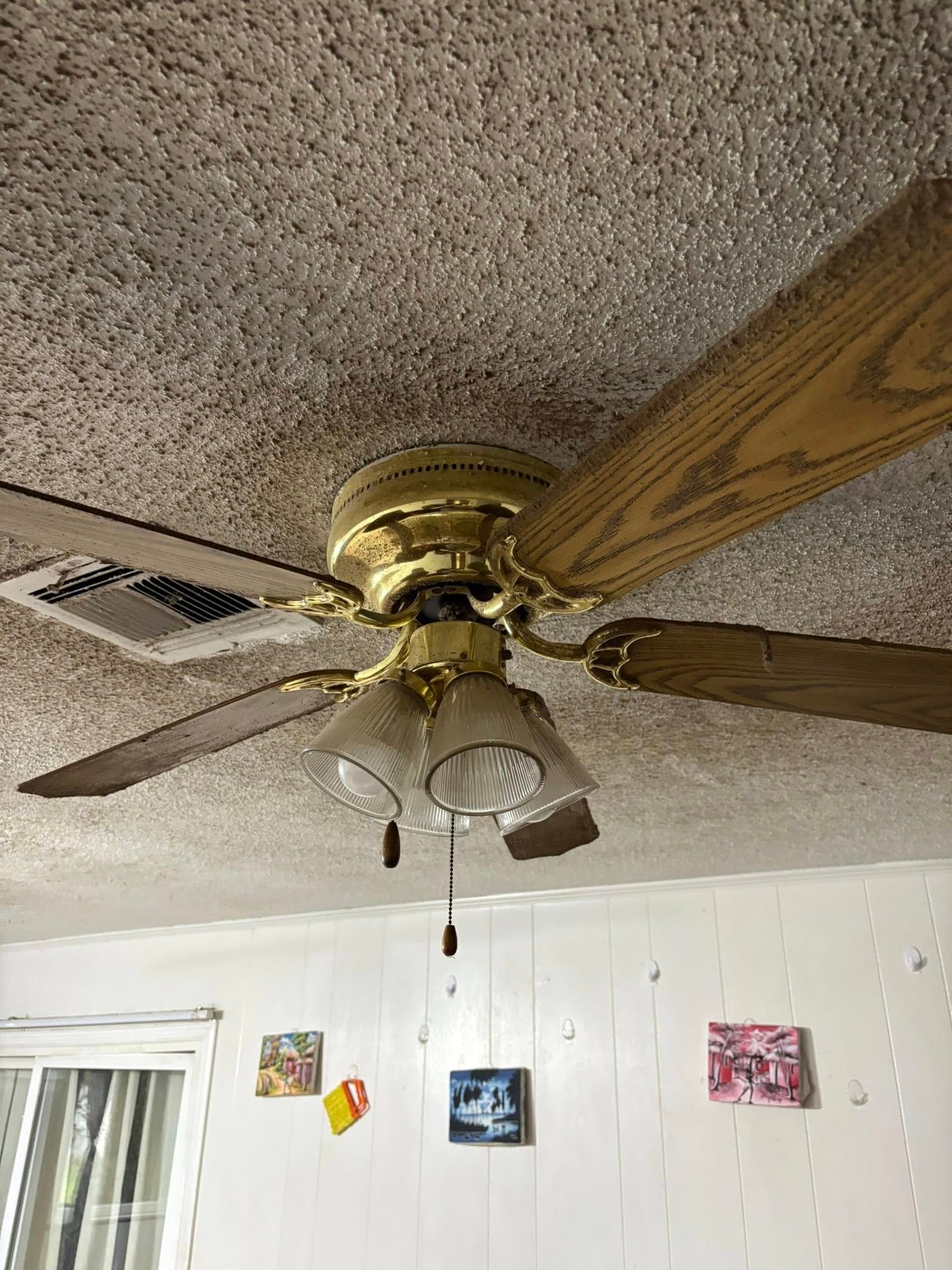 Ceiling fan with gold finish and wood blades, mounted on textured ceiling. Three-light fixture.