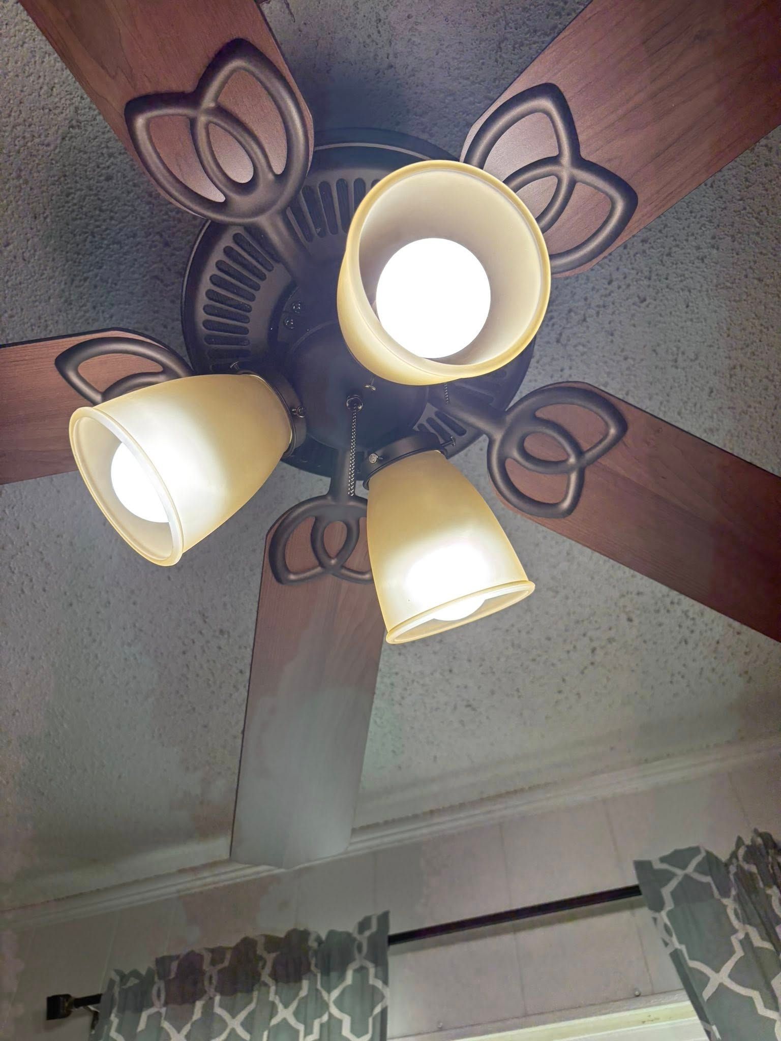 Ceiling fan with three lights, brown blades, and decorative metal accents.