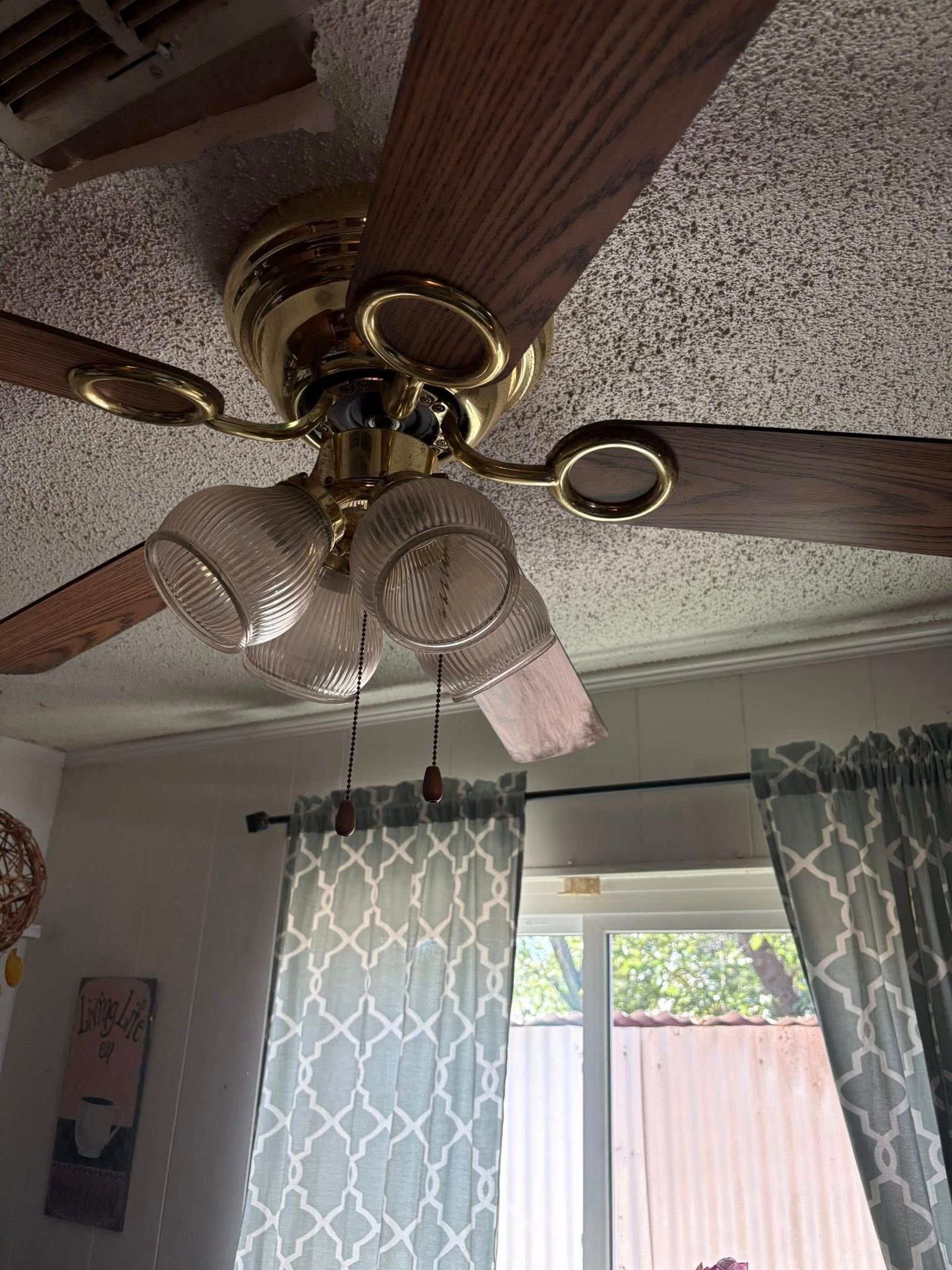 Ceiling fan with gold finish and wooden blades, glass light fixtures, mounted on textured ceiling.