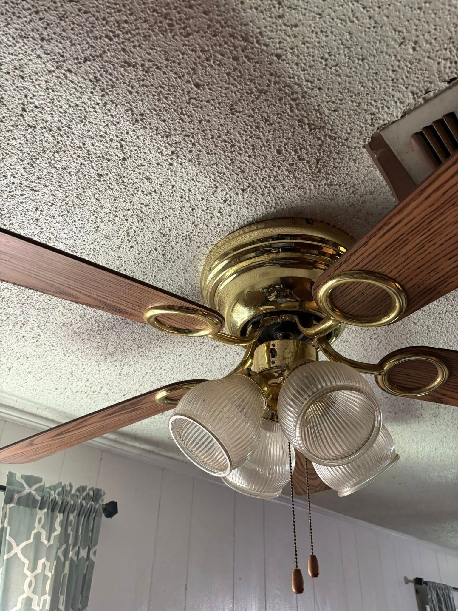 Ceiling fan with gold finish, wood blades, three glass light fixtures, mounted on textured ceiling.