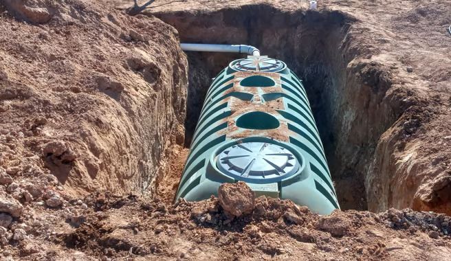 A large green tank is sitting in a hole in the dirt.