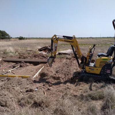 A small excavator is digging a hole in the dirt in a field.