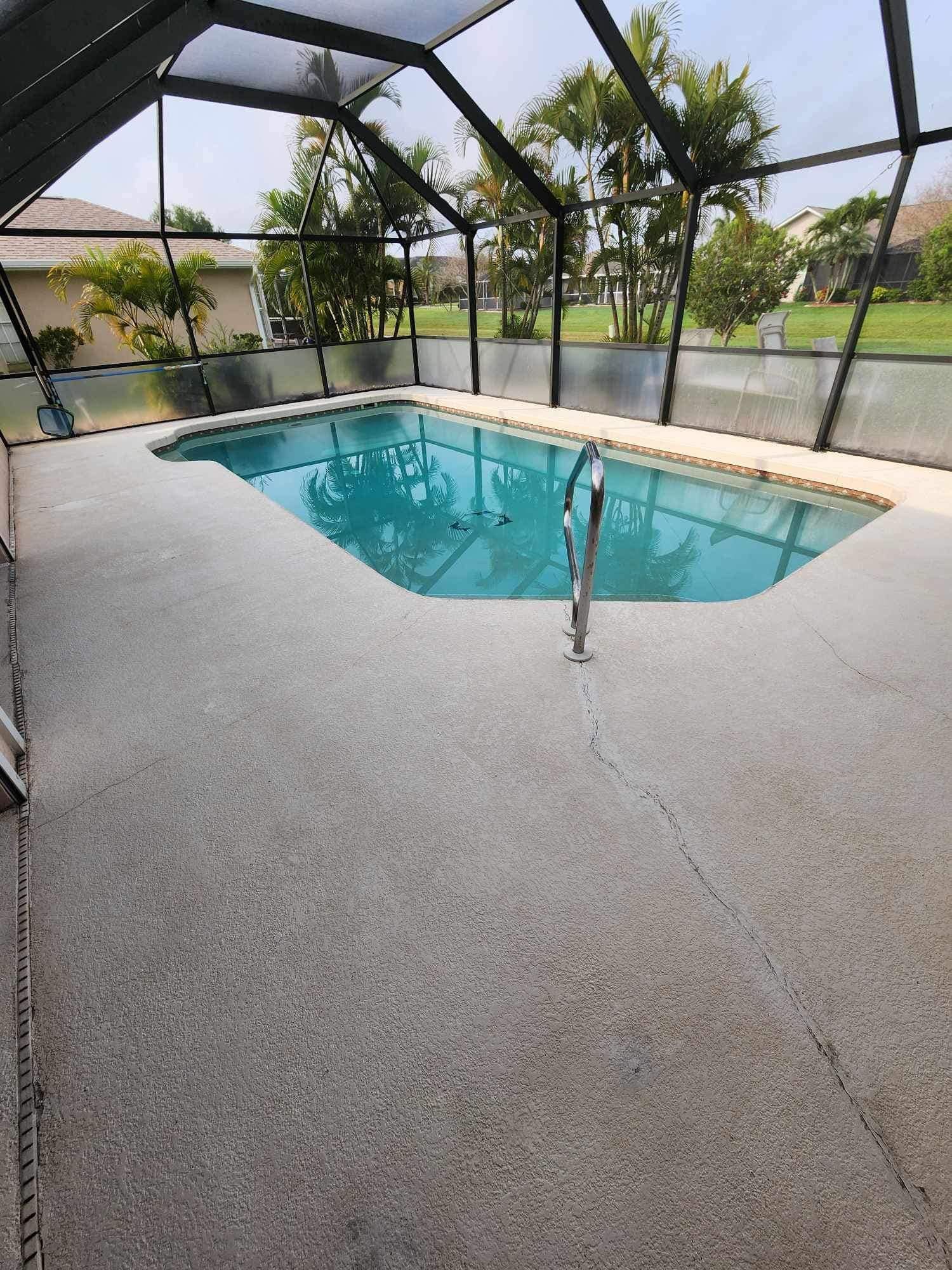 A large swimming pool is surrounded by a screened in area.