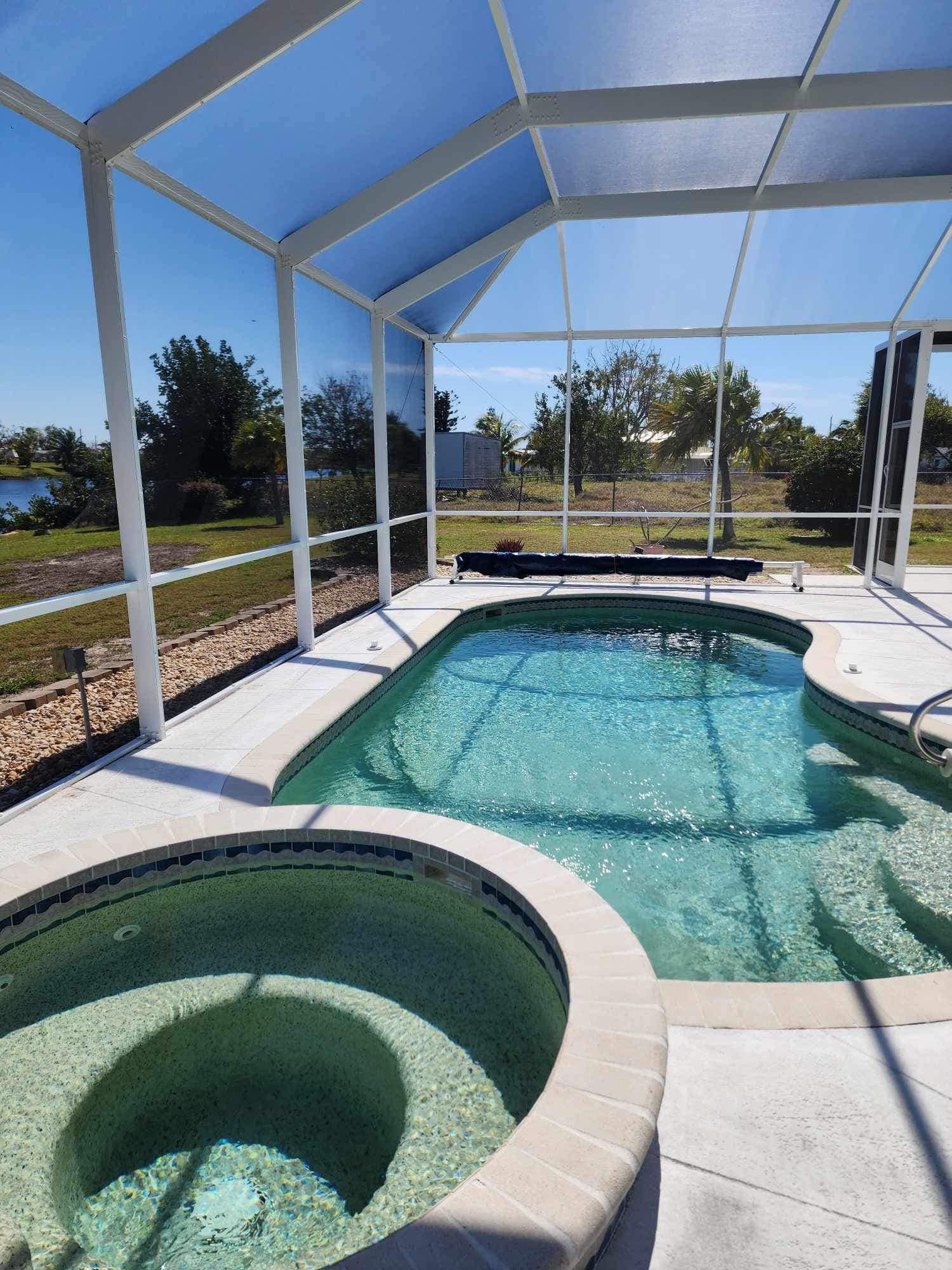 A swimming pool with a hot tub surrounded by a screened in area.