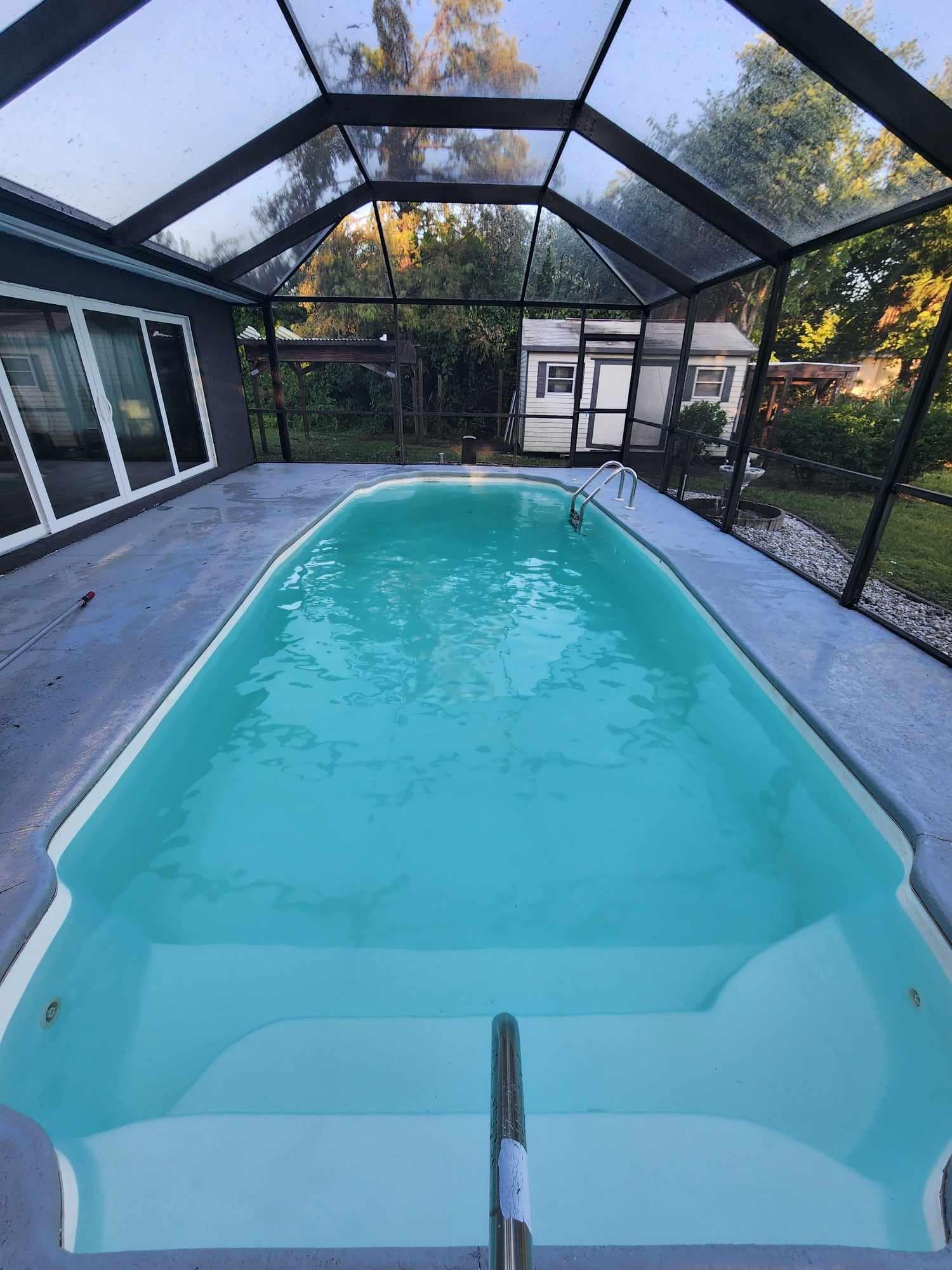 A large swimming pool covered in a screened in area with a house in the background.
