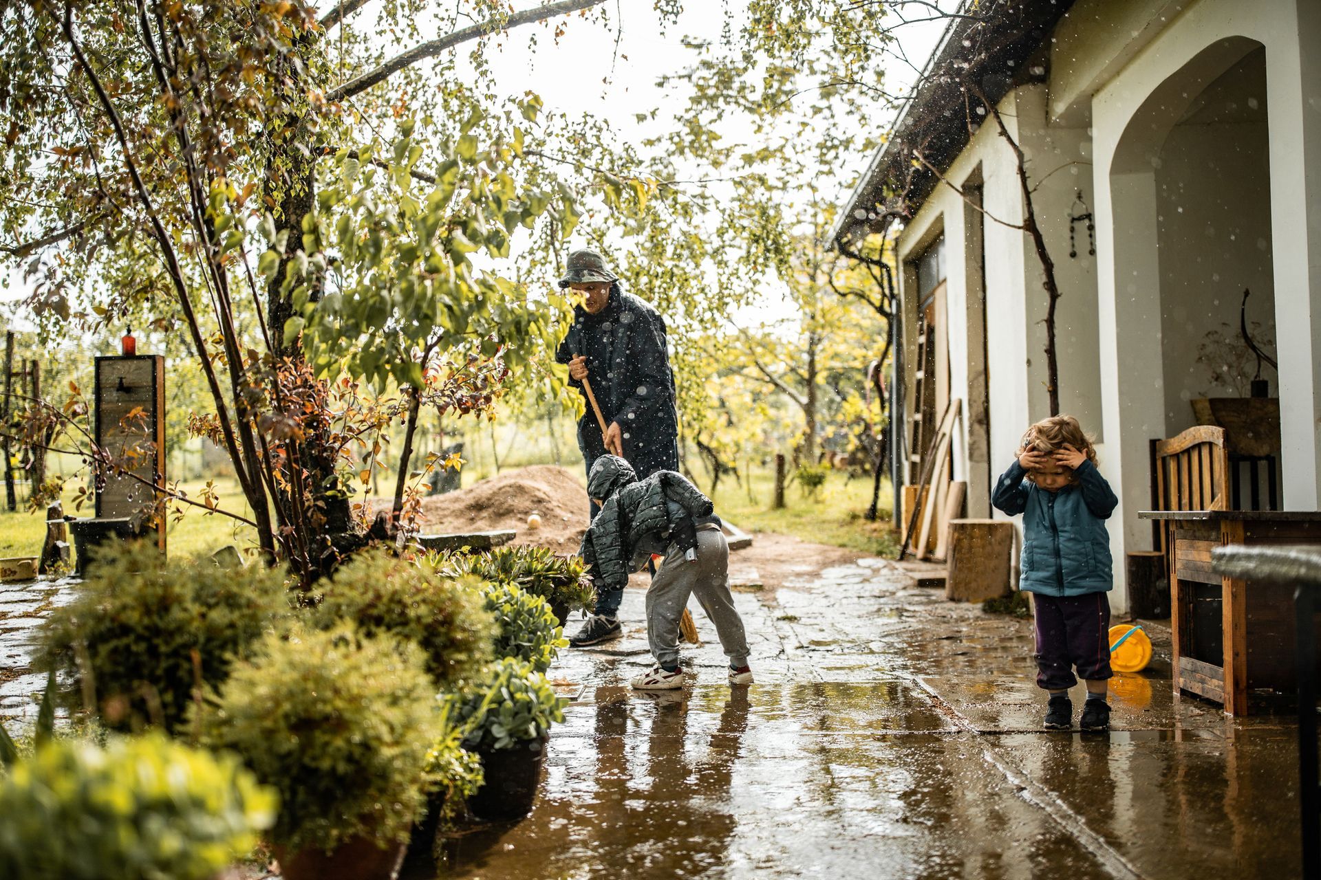 A man and two children are playing in the rain on a patio.