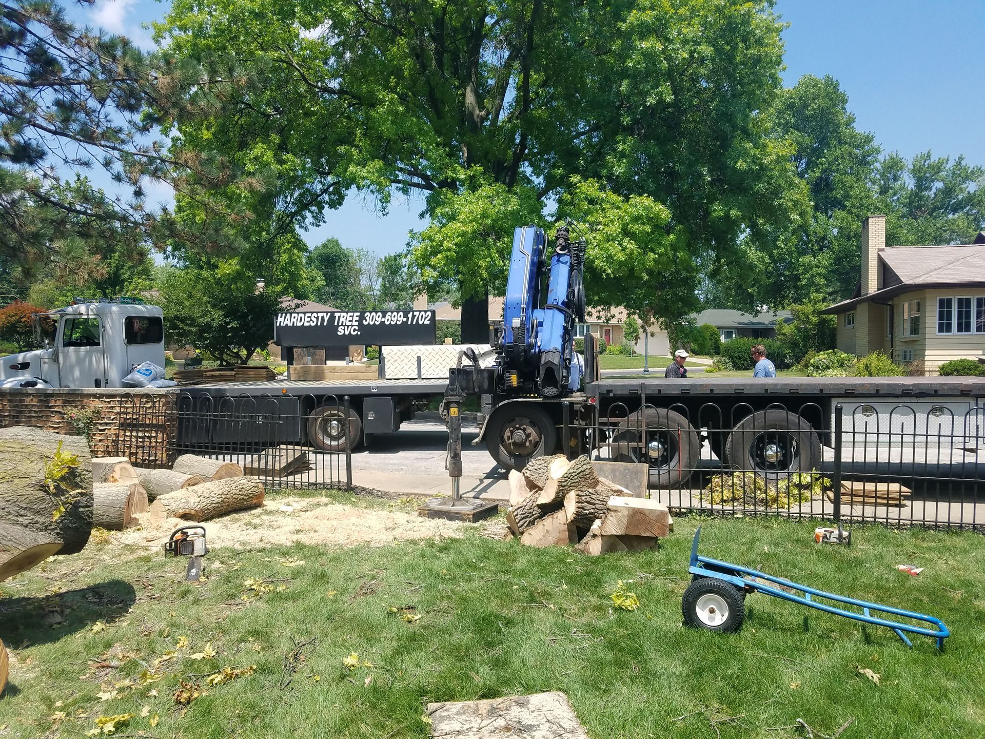 A truck with a crane on the back is carrying logs in a yard.