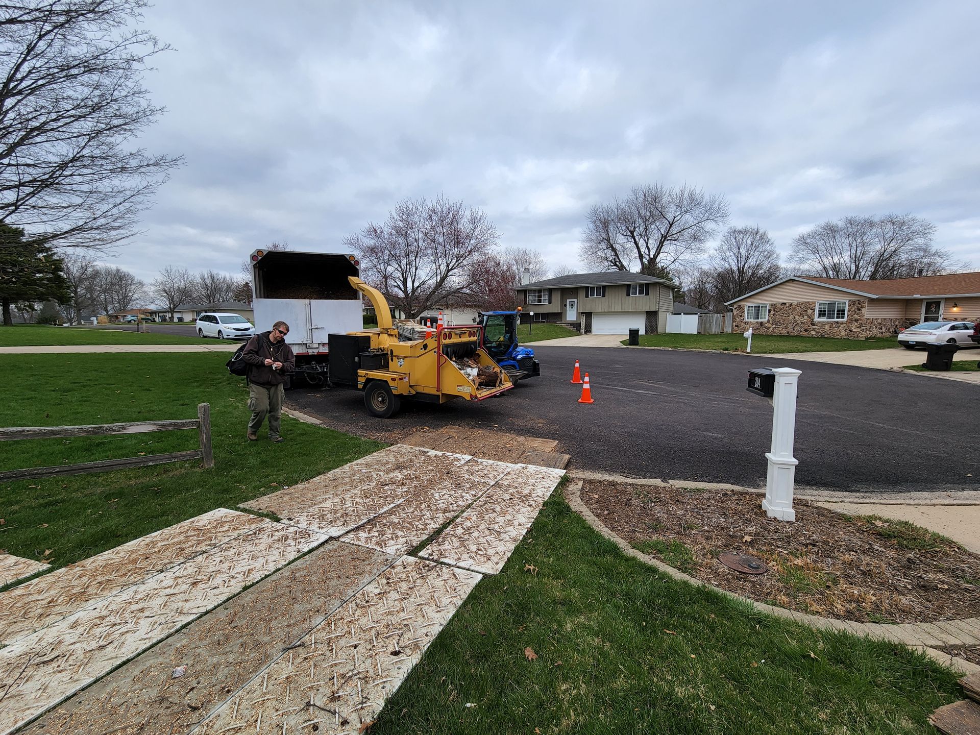 A man is standing next to a tree chipper in a driveway.