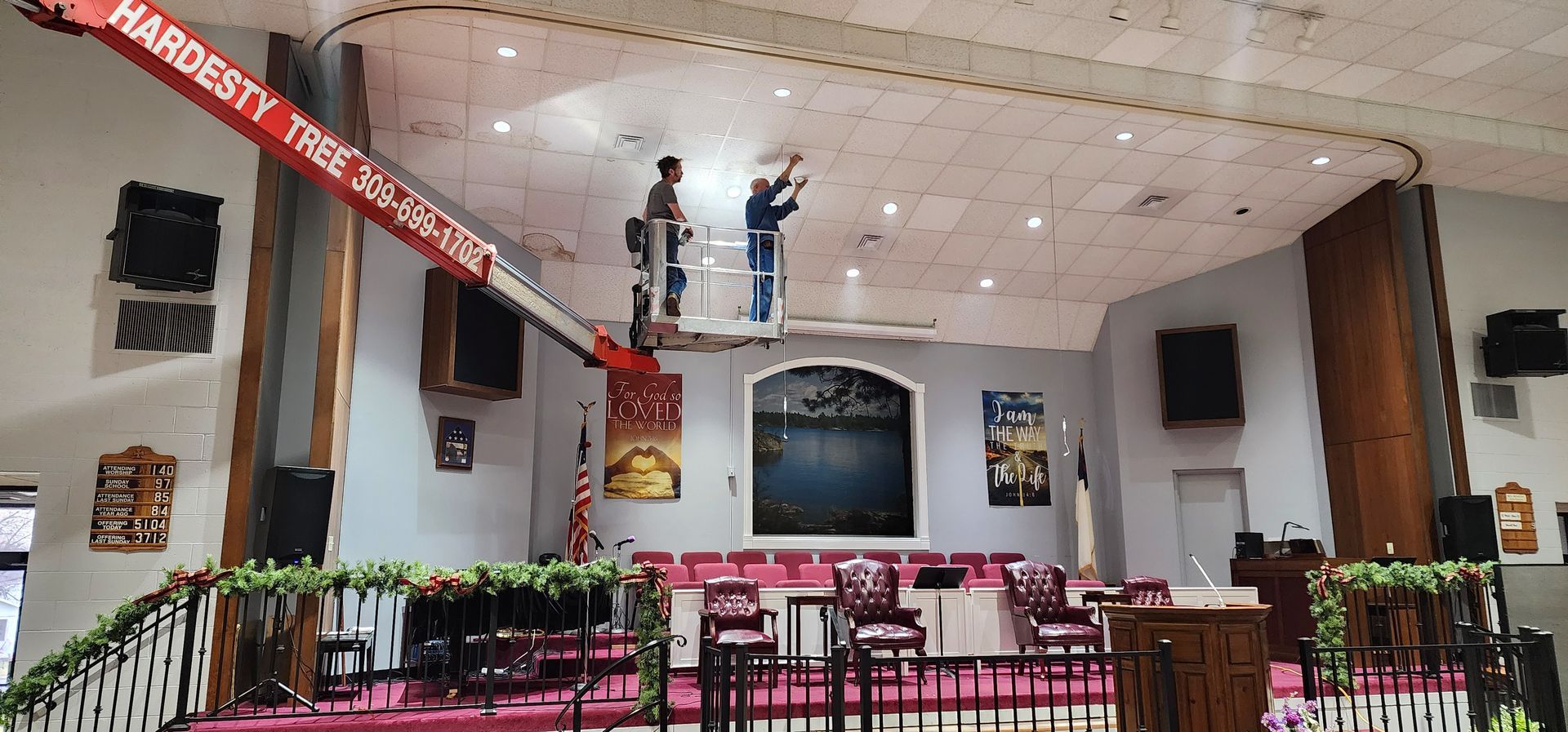 Two men are working on the ceiling of a church with a crane.