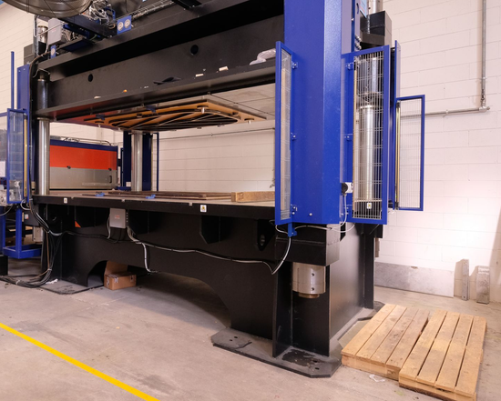 Un grande macchinario è parcheggiato in un magazzino accanto a pallet di legno.