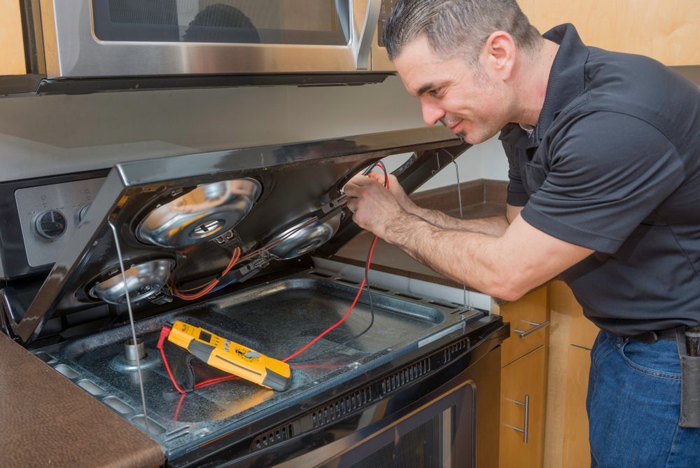 Man Repairing a Black Electric Stove With a Multimeter in a Kitchen — Holders Electrical In Warwick, QLD