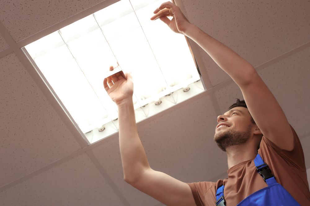 Man Reaching Into a Ceiling Light Fixture, Smiling, in a Room  — Holders Electrical In Tenterfield, NSW 
