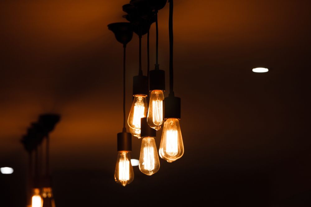 Exposed Edison Bulb Chandelier Illuminates a Dark Setting With Warm, Orange Light — Holders Electrical In Tenterfield, NSW