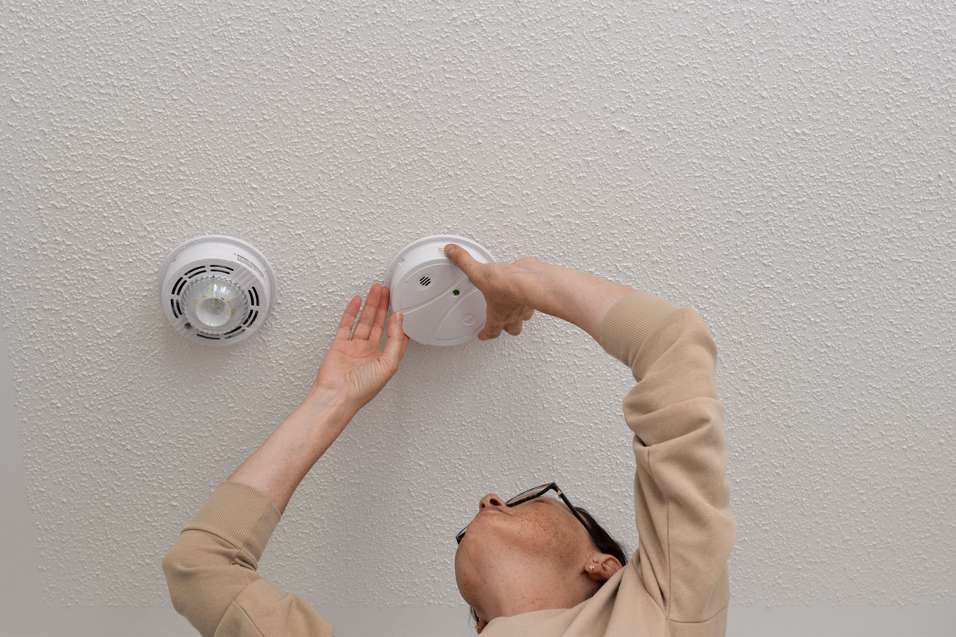 Person Installing a Smoke Detector on a Textured White Ceiling  — Holders Electrical In Tenterfield, NSW 