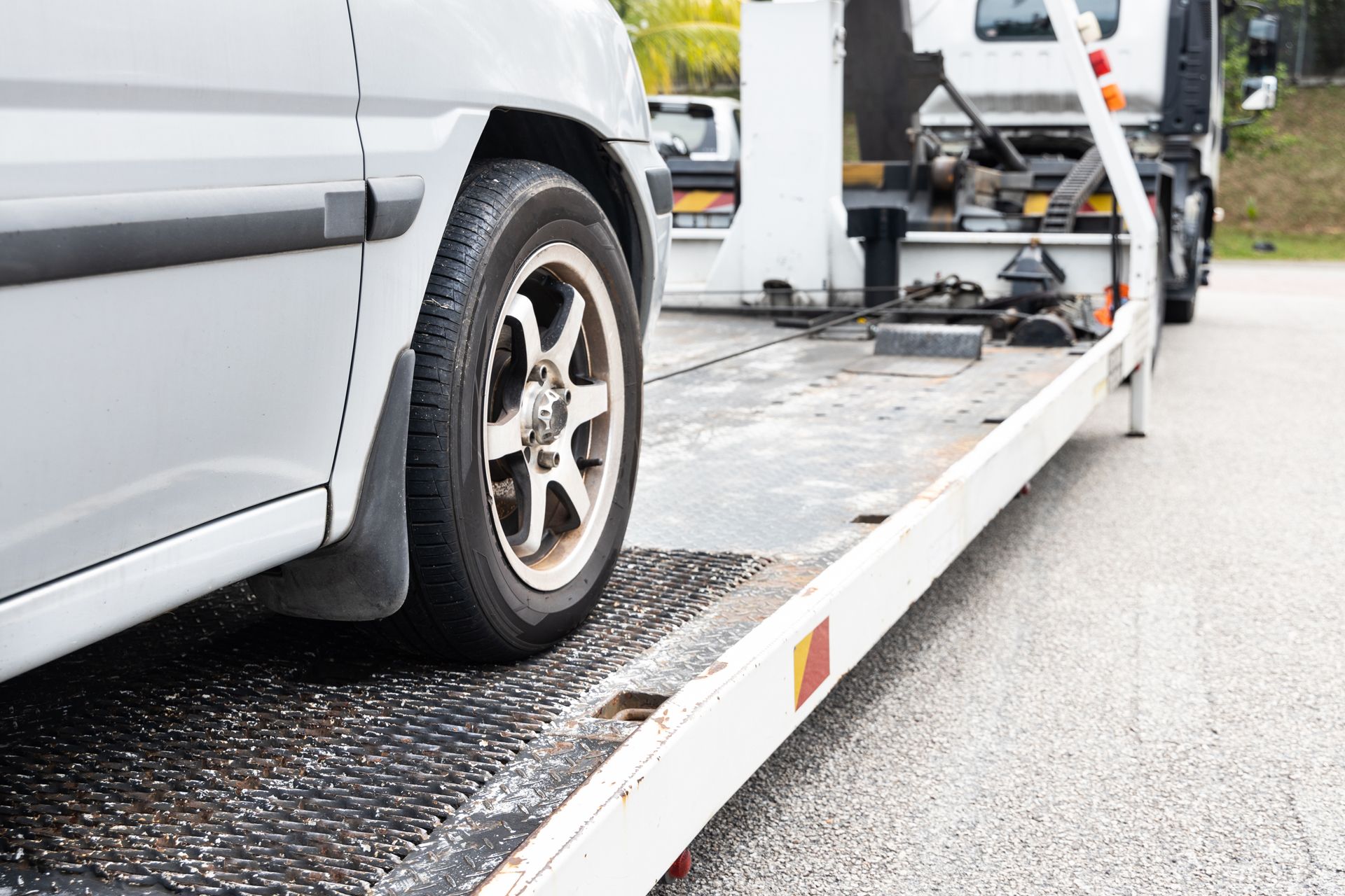 Silver car being loaded onto a tow truck flatbed on a wet road