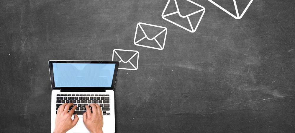 A person is typing on a laptop in front of a blackboard with envelopes drawn on it.