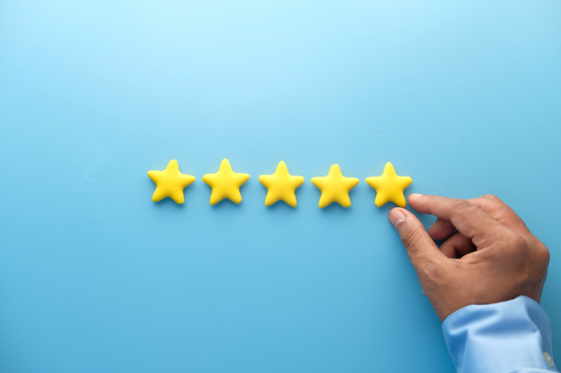 Hand placing a fifth yellow star beside four stars on a blue background