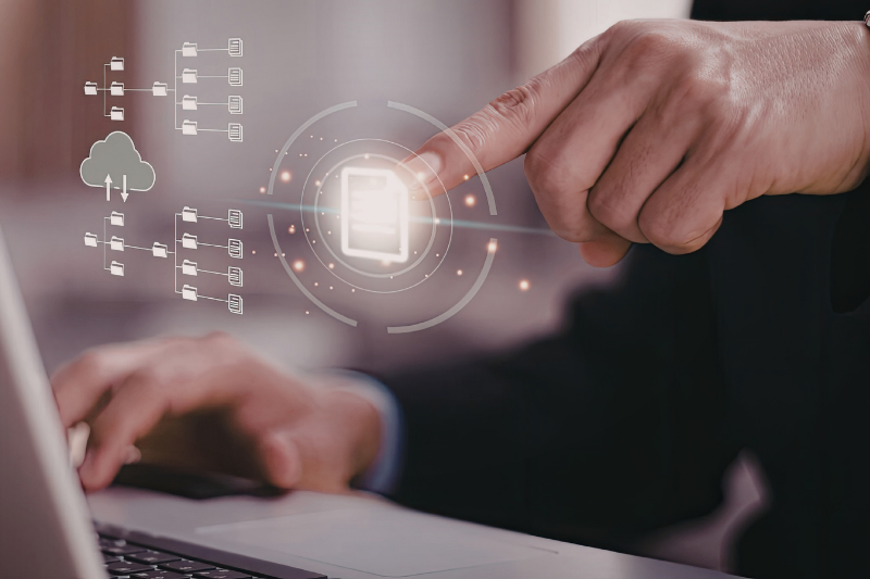 A person using a laptop with a digital holographic overlay of file management icons and a cloud storage symbol.