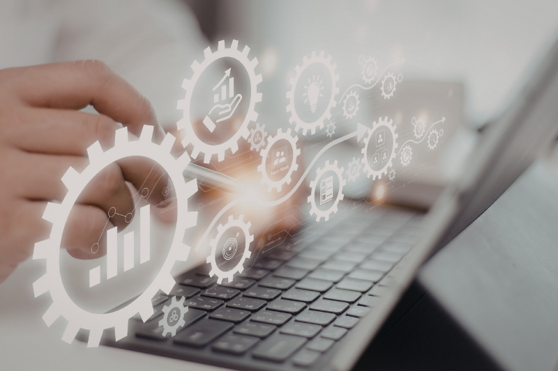 A person typing on a laptop with a digital overlay of interconnected glowing gears displaying business icons.