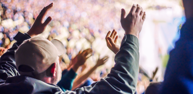 A crowd of people are raising their hands in the air at a concert.
