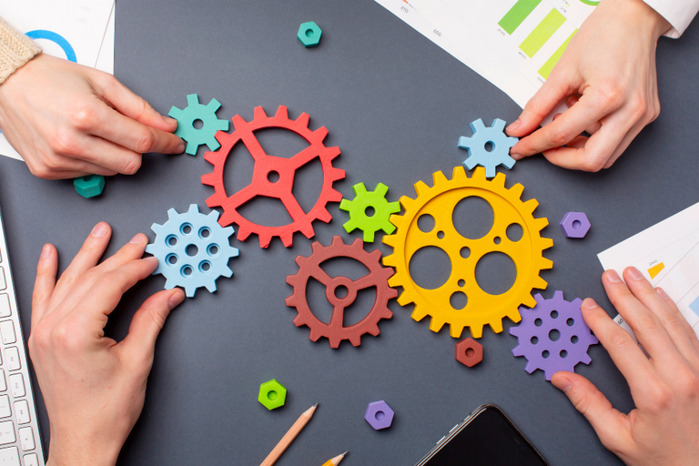 Hands arranging colorful gear-shaped puzzle pieces on a desk with charts and a keyboard.
