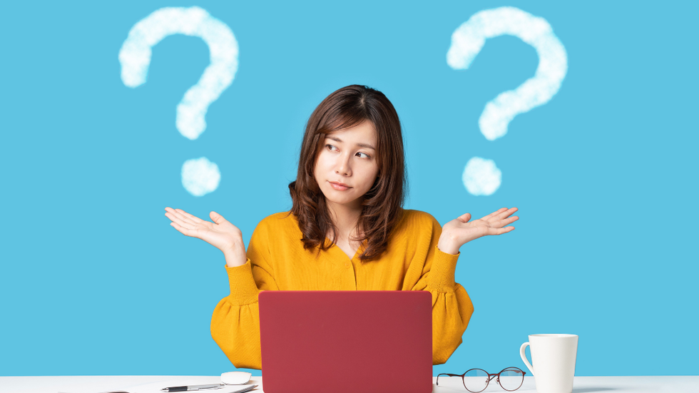 Woman with outstretched hands, looking puzzled, in front of a laptop, question marks above her.