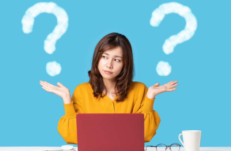 Woman with outstretched hands, looking puzzled, in front of a laptop, question marks above her.