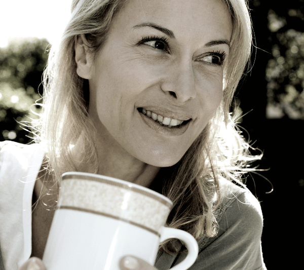 A woman is smiling while holding a cup of coffee