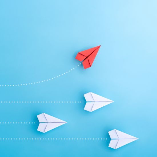 a red paper airplane is leading three white paper airplanes on a blue background .