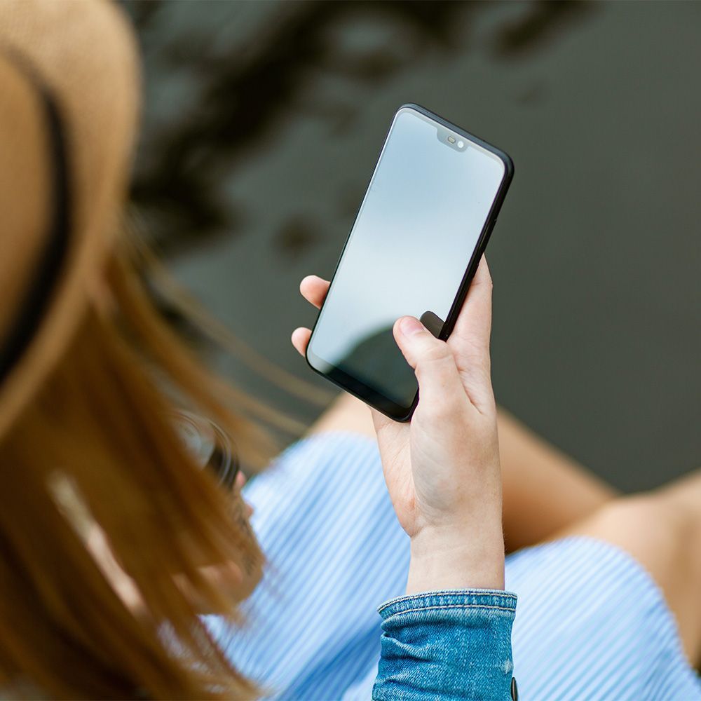 a woman wearing a hat is holding a cell phone in her hand .