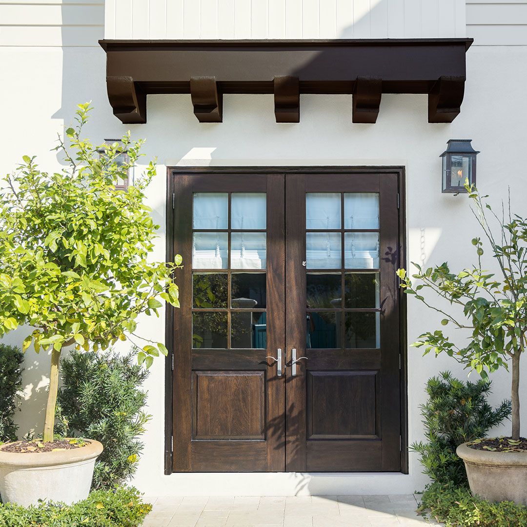 A white house with a brown door and potted plants in front of it