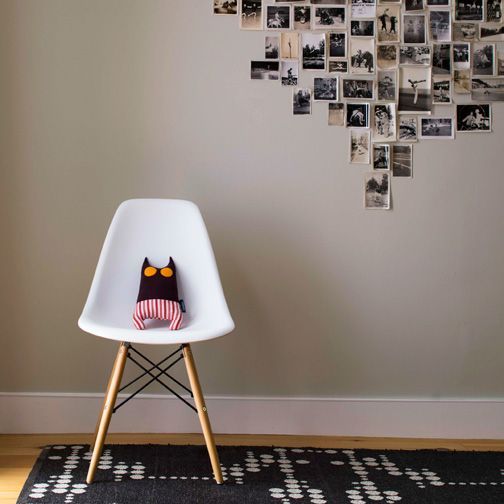 A stuffed cat is sitting on a chair in front of a wall full of pictures