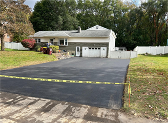 Freshly paved asphalt driveway in front of a house, with caution tape.