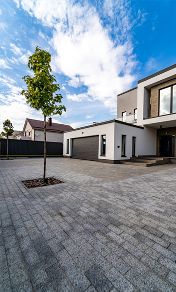 Modern white house with gray driveway, tree, and garage against a blue sky with clouds.