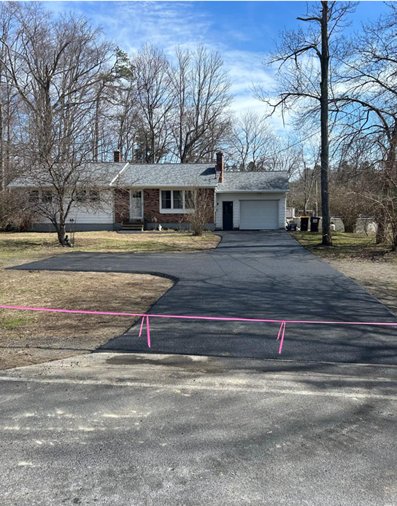 A one-story home with a newly paved driveway. Pink tape blocks off access.