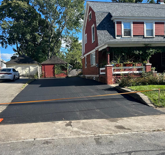 Asphalt driveway in front of a red house, with a garage and a car.