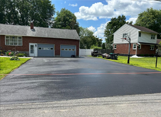 Newly paved asphalt driveway in front of a brick house with a garage and a two-story house with a basketball hoop.