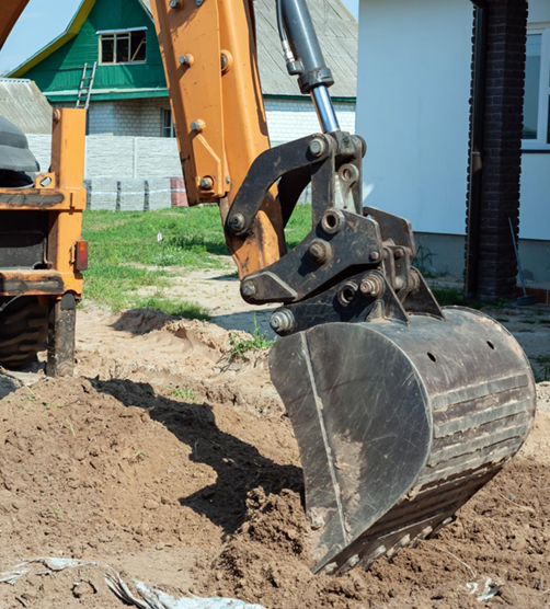 Excavator bucket digging into the ground; orange and black machine with a house in the background.