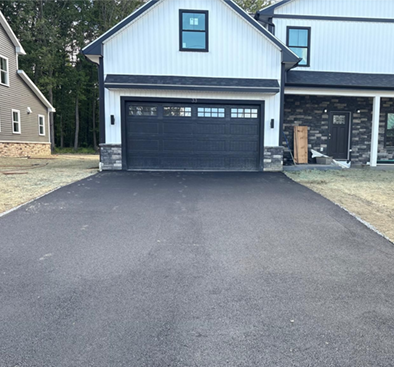 Black asphalt driveway leading to a modern two-story home with a black garage door and white siding.