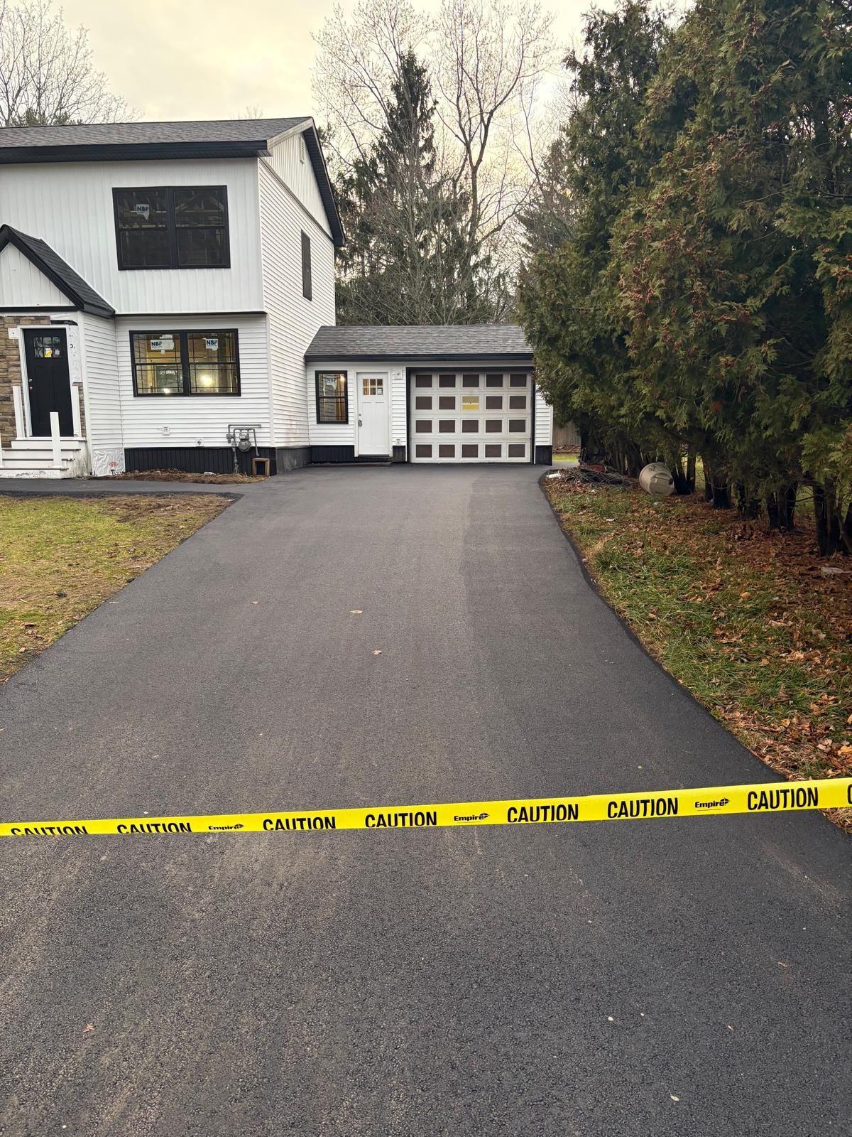 Asphalt driveway with caution tape in front of a two-story white house and garage.