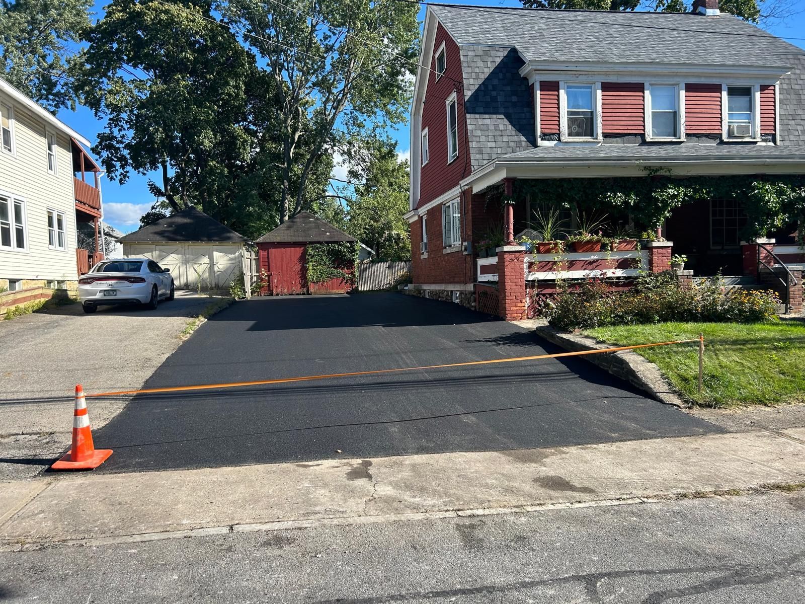 Newly paved asphalt driveway in front of a red house, orange traffic cone on the side.