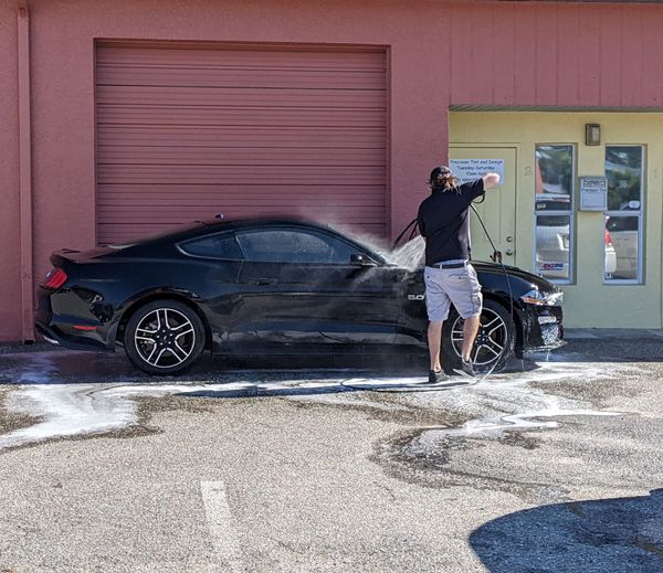 A person is cleaning a blue car with an orange towel