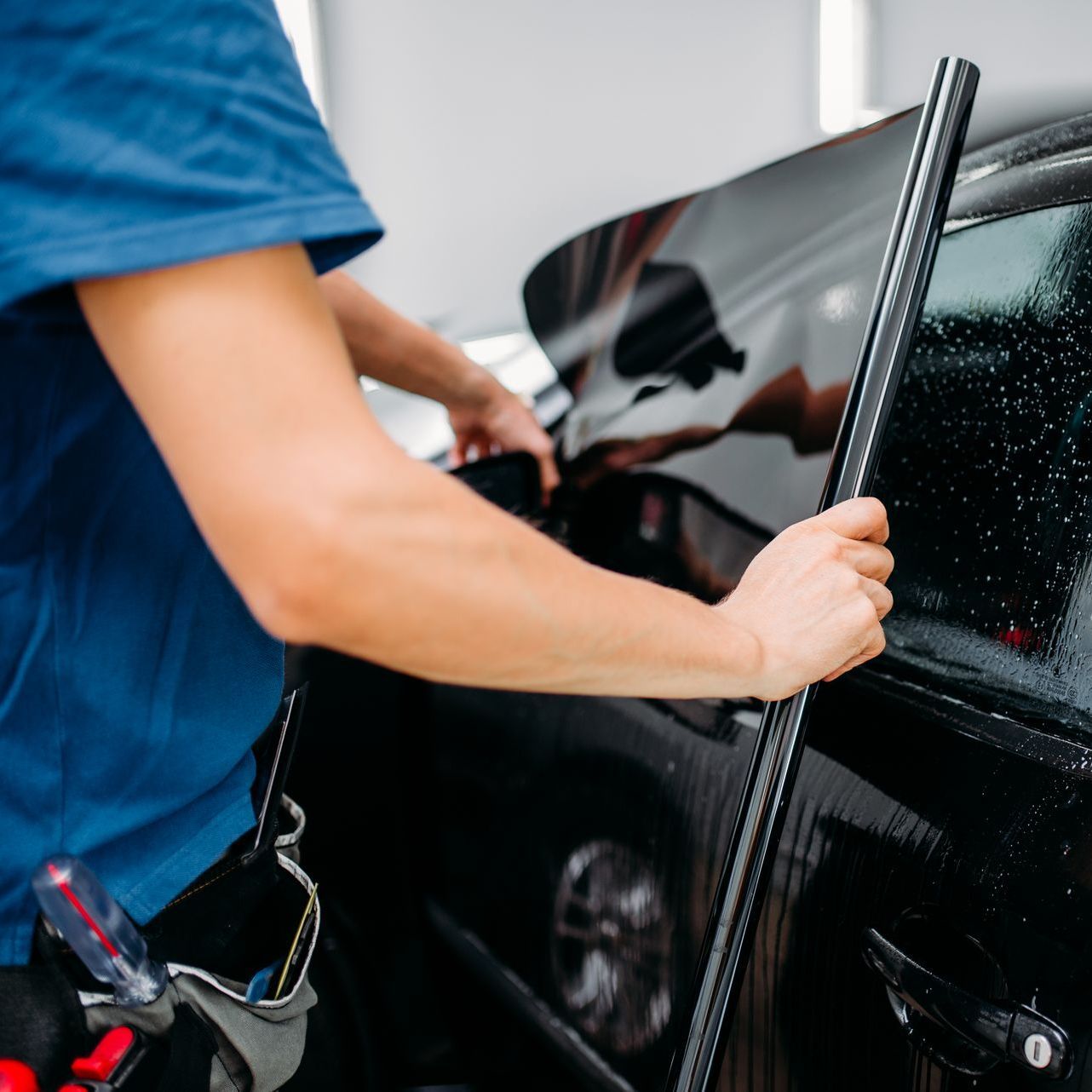 A man is applying window tinting to a black car.