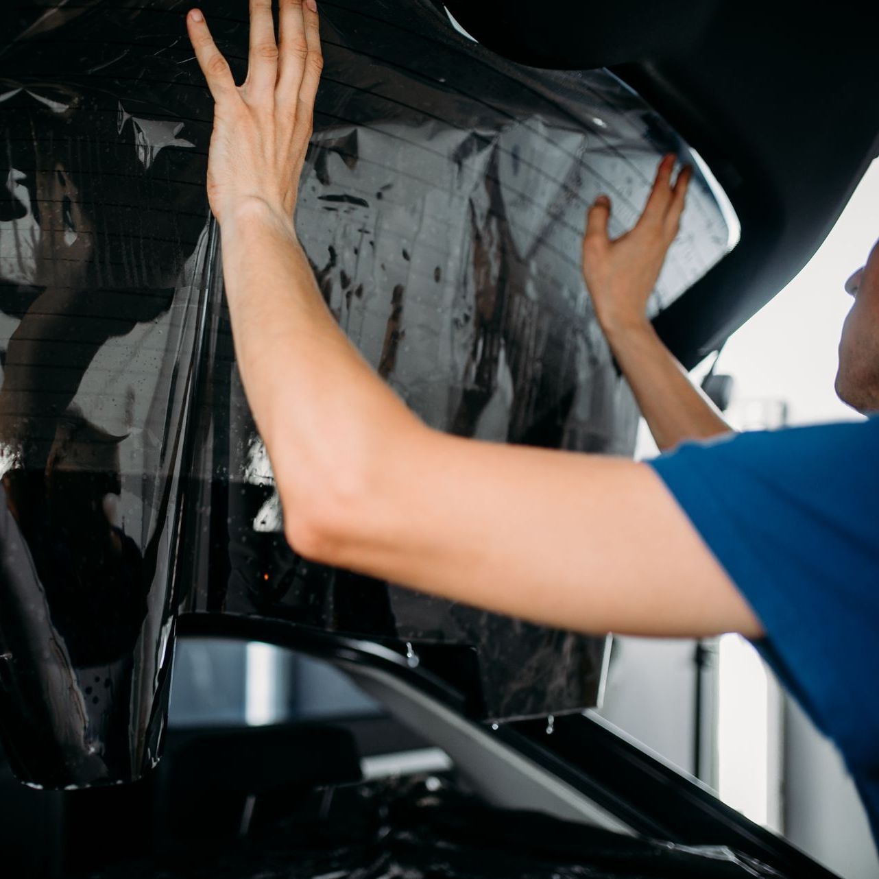 A man is applying tinted glass to the hood of a car.