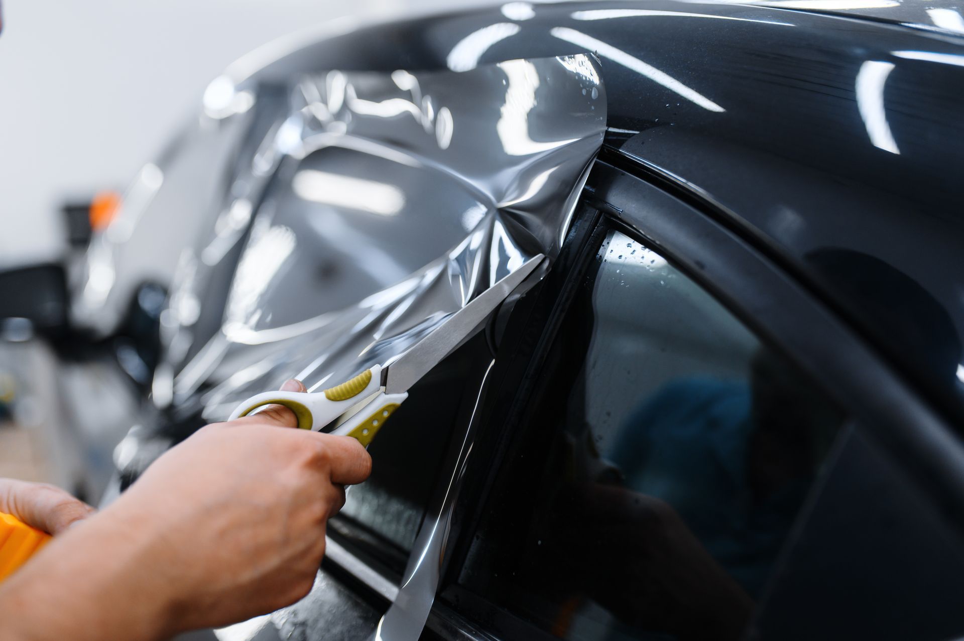 A person is cutting a piece of tinted film on a car window.