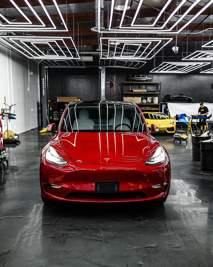 A red tesla model 3 is parked in a garage.