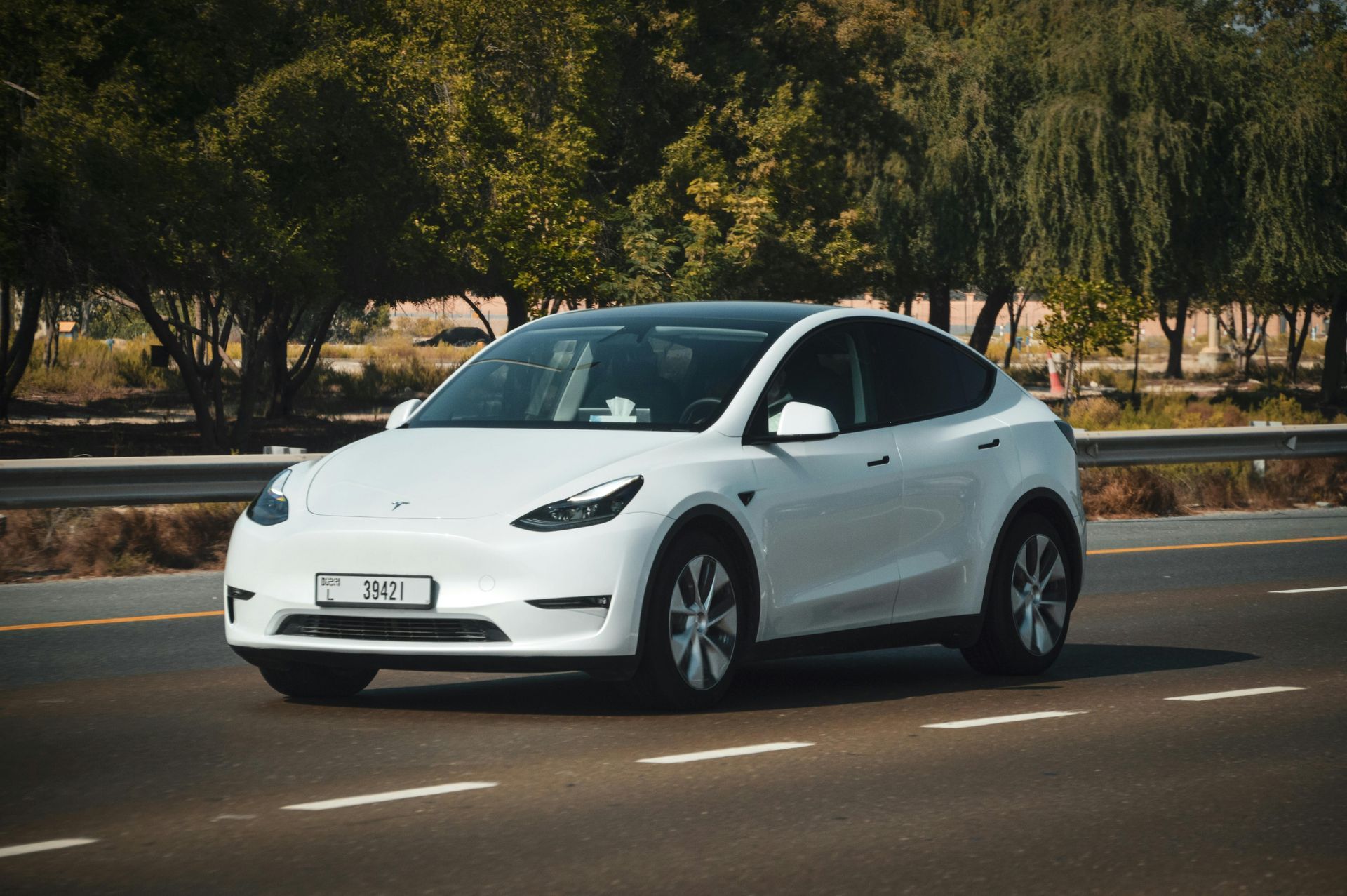 A white tesla model y is driving down a highway.